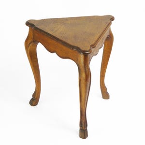 Puede incluir: Una mesa de madera triangular con tres patas. La mesa tiene un acabado marrón oscuro y tallas intrincadas en las patas.