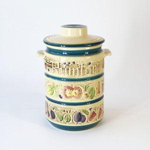 May include: A ceramic jar with a lid, decorated with a blue, green and yellow fruit pattern. The jar has the word "Rumtopf" written on it.