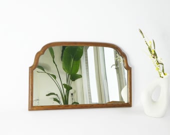 May include: A wooden framed arched mirror with a bevelled edge. The mirror reflects a plant and a window.