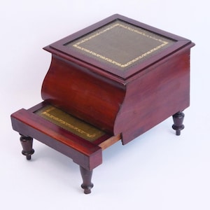 May include: A wooden step stool with a hinged top. The top is covered in green leather with a gold trim. The stool has four turned legs.