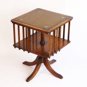 May include: A wooden revolving book stand with a leather top and a decorative base. The stand has a square top and a round base.