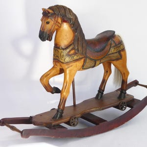 May include: A vintage wooden rocking horse with a tan body, brown mane, and a dark saddle. The horse has decorative gold accents and is mounted on a red wooden base with wheels. A classic toy.