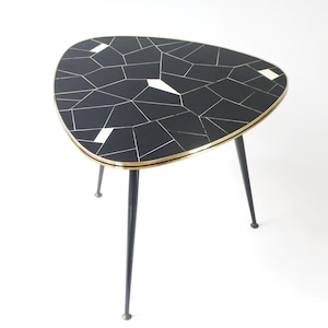 Può includere: Un tavolino triangolare moderno della metà del secolo. Il piano del tavolo presenta un design a mosaico nero con accenti bianchi e dorati. Il tavolo ha tre gambe in metallo nero con punte color ottone. Il tavolo è largo circa 61 cm.