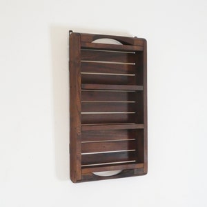 Op de afbeelding: Een donkerbruin houten wandrek met drie planken. Het rek heeft een eenvoudig ontwerp met afgeronde randen en is gemonteerd op een witte muur.