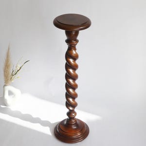 Op de afbeelding: Een hoge, donkerbruine houten standaard met een rond blad, een centrale kolom met een opvallend spiraalvormig ontwerp en een brede, getrapte ronde voet. De standaard heeft een gladde, gepolijste afwerking en staat rechtop.