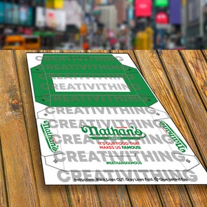 K&ouml;nnte beinhalten: Eine druckbare Vorlage f&uuml;r eine Nathan's Famous Hotdog-Box. Die Vorlage ist wei&szlig; mit schwarzen Schnittlinien und grauen Faltlinien. Die Vorlage zeigt das Nathan's Famous Logo und den Text "It's our food that makes us famous!" mit dem Hashtag #NATHANSFAMOUS.