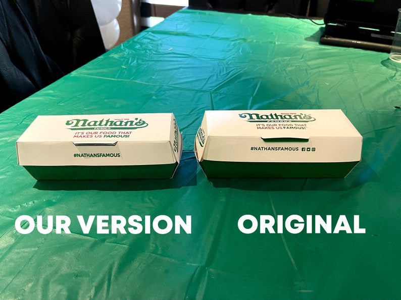 K&ouml;nnte beinhalten: Zwei wei&szlig;e und gr&uuml;ne Nathan's Famous Hotdog-Boxen nebeneinander auf einem gr&uuml;nen Tischtuch. Die Box auf der linken Seite hat den Text "IT'S OUR FOOD THAT MAKES US FAMOUS!" und den Hashtag "#NATHANSFAMOUS". Die Box auf der rechten Seite hat den Text "IT'S OUR FOOD THAT MAKES US FAMOUS" und den Hashtag "#NATHANSFAMOUS". Der Text "OUR VERSION" befindet sich unter der linken Box und der Text "ORIGINAL" unter der rechten Box.