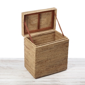 May include: A woven wicker storage trunk with a hinged lid and leather straps. The lid is open, revealing the empty interior of the trunk.