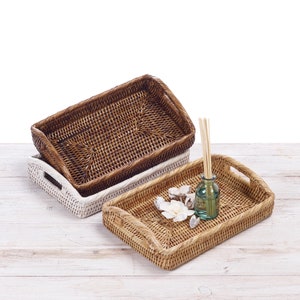 May include: Two woven wicker trays, one brown and one white, with a small glass bottle and decorative items on the brown tray.
