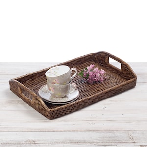May include: A brown wicker tray with two teacups and a saucer, and a small bunch of pink flowers.