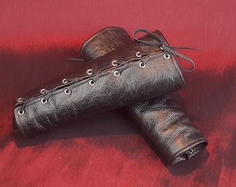 May include: A pair of black leather arm guards with laces and metal eyelets. The guards are tied together with a black ribbon.