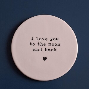 May include: White ceramic coaster with the text "I love you to the moon and back" in black lettering and a small black heart.