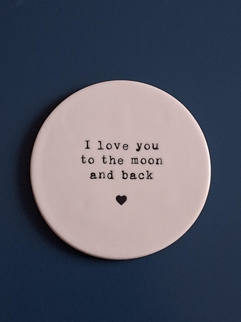 May include: White ceramic coaster with the text "I love you to the moon and back" in black lettering and a small black heart.
