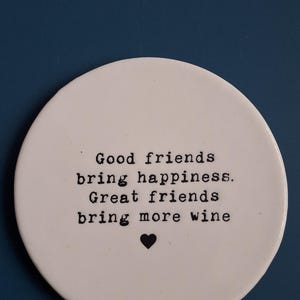 May include: White ceramic coaster with black text that reads "Good friends bring happiness. Great friends bring more wine" and a small black heart.