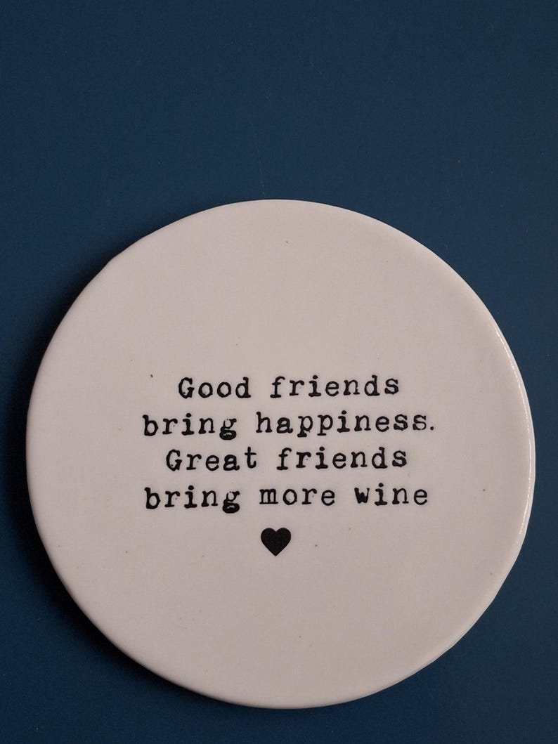 May include: White ceramic coaster with black text that reads "Good friends bring happiness. Great friends bring more wine" and a small black heart.