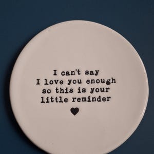 May include: White ceramic dish with black text that reads "I can't say I love you enough so this is your little reminder" with a small black heart.