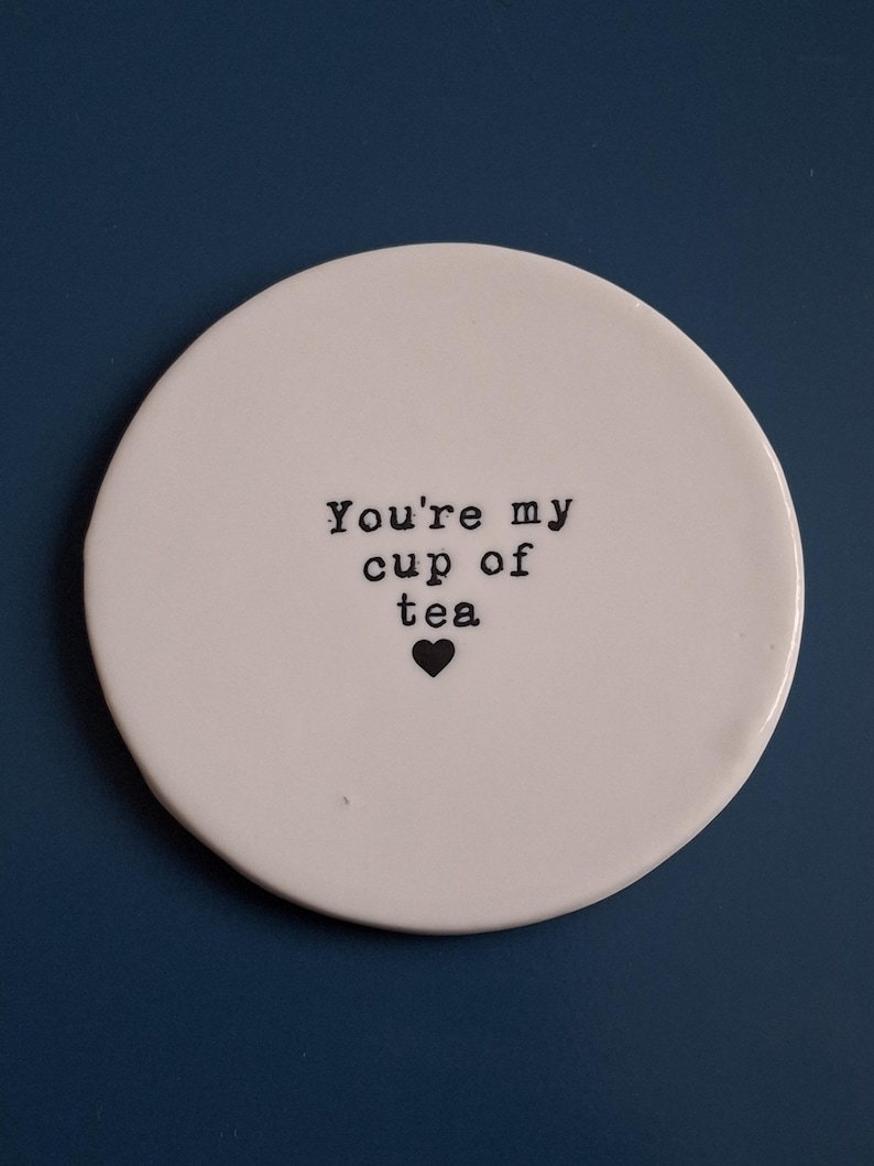 May include: White ceramic coaster with the text "You're my cup of tea" and a small black heart.