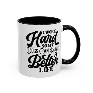 May include: White ceramic coffee mug with a black rim and handle. The mug has a black graphic that reads "I work hard so my dogs can have a better life."