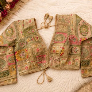 May include: A long-sleeved blouse featuring a patchwork design with intricate embroidery in shades of gold, green, and pink. The garment has a deep V-neckline, a front tie closure with tassels, and is embellished with small reflective sequins throughout.