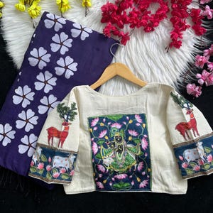 Puede incluir: Blusa color crema con bordados de ciervos y motivos florales. Cuenta con un panel azul marino y verde con una figura de deidad y flores de loto. Tambi&eacute;n hay una tela azul marino a juego con dise&ntilde;os florales blancos.