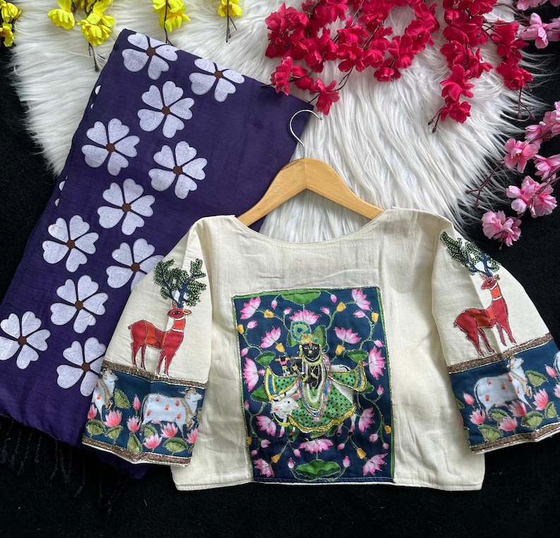 Puede incluir: Blusa color crema con bordados de ciervos y motivos florales. Cuenta con un panel azul marino y verde con una figura de deidad y flores de loto. Tambi&eacute;n hay una tela azul marino a juego con dise&ntilde;os florales blancos.