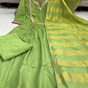May include: A lime green Indian salwar kameez set. The dress features a round neckline with silver and gold embellishments, a pink trim, and a matching dupatta with gold stripes. The set includes a matching pair of pants.