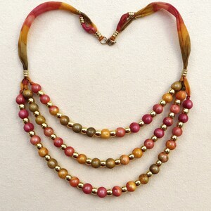 May include: A three-strand necklace with gold and brown beads. The necklace is made of silk and has a clasp closure.