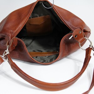 May include: A brown leather handbag with a single strap and a small pocket on the inside. The bag is open and the inside is visible.