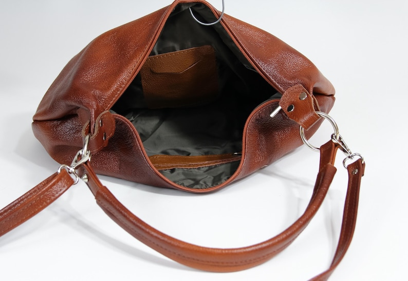 May include: A brown leather handbag with a single strap and a small pocket on the inside. The bag is open and the inside is visible.
