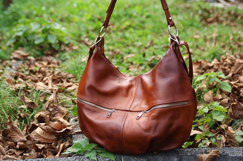 May include: A brown leather hobo bag with silver hardware and zipper closures. The bag has a slouchy, casual look and is perfect for everyday use.
