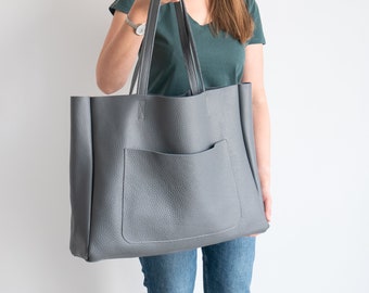 May include: A large grey tote bag with a front pocket. The bag has a textured leather-like finish.