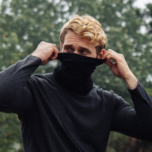 May include: A person wearing a black mock neck shirt and a black neck gaiter. The person is adjusting the neck gaiter with their hands.
