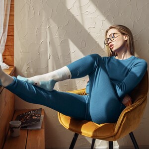 May include: A long-sleeved blue thermal shirt and matching blue thermal leggings worn with white and light blue socks featuring black text on the cuffs. The socks have a reinforced heel and toe design in a light blue color, paired with the blue set.