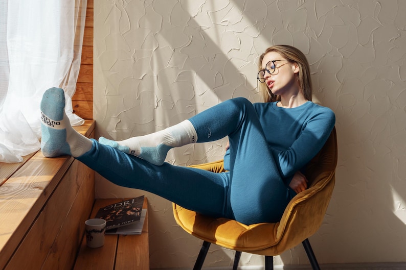 May include: A long-sleeved blue thermal shirt and matching blue thermal leggings worn with white and light blue socks featuring black text on the cuffs. The socks have a reinforced heel and toe design in a light blue color, paired with the blue set.