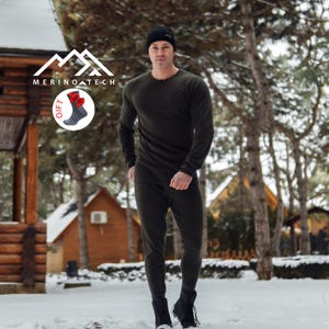 May include: A dark olive green long-sleeve thermal shirt and matching thermal pants set. The outfit includes a black beanie and a circular graphic featuring a pair of gray socks with red accents and the text MERINO TECH.