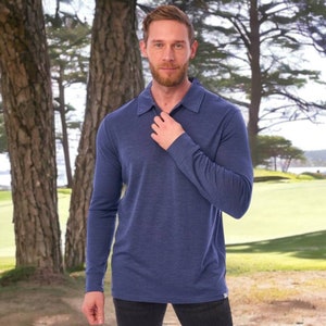 May include: A long-sleeved, navy blue polo shirt with a collared neckline. The shirt is made of a soft, textured fabric and is being worn outdoors. The background features trees and a golf course.