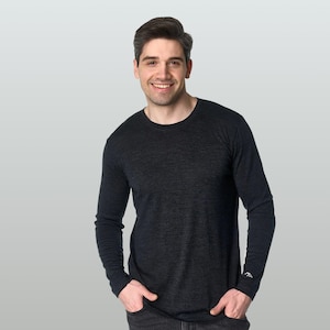 May include: A long-sleeve crew neck shirt in a dark charcoal heathered fabric. The shirt features a small white mountain range logo embroidered on the left sleeve cuff. The garment has a simple, solid-colored design with long sleeves and a round neckline.