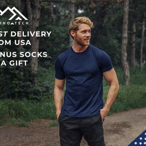 May include: A man wearing a dark blue t-shirt and black pants stands in a forest. The text "FAST DELIVERY FROM USA BONUS SOCKS AS A GIFT" is displayed above him. A small American flag is in the lower right corner of the image.