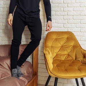 May include: A pair of solid black thermal long johns featuring a ribbed texture, a fitted waistband, and cuffed ankles. The garment is worn with a matching black long-sleeved shirt and gray patterned socks, providing a full-length view of the pants.