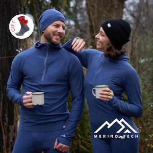 Può includere: Due persone indossano berretti blu e neri e maglie a maniche lunghe blu abbinate con zip al collo. La maglia blu presenta una cerniera e fori per i pollici. Un piccolo grafico circolare mostra una calza grigia con un fiocco rosso.