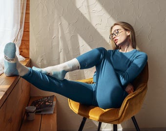 May include: A long-sleeved blue thermal shirt and matching blue thermal leggings worn with white and light blue socks featuring black text on the cuffs. The socks have a reinforced heel and toe design in a light blue color, paired with the blue set.