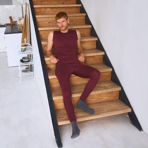 May include: A burgundy sleeveless shirt and matching leggings are worn by a person sitting on wooden stairs. The outfit is made of a soft, textured material. The person is also wearing gray socks.