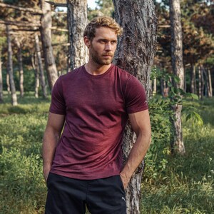 May include: A short-sleeved crew neck t-shirt in a heathered maroon color with a small white logo on the left sleeve, paired with black athletic shorts. The t-shirt features a standard fit and a textured fabric appearance throughout the garment.
