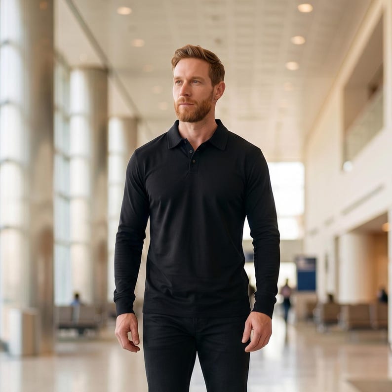 May include: A black long-sleeve polo shirt with a collared neckline and button closure. The shirt is made of a smooth, solid-colored fabric. The person is wearing black pants.