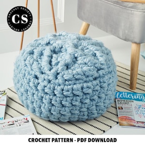 May include: A light blue crochet footstool with a textured surface. The footstool is sitting on a black and white striped rug.