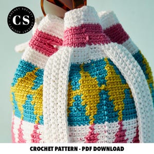 Pu&ograve; includere: Una borsa a uncinetto con un motivo geometrico rosa, bianco, giallo e blu. La borsa ha una tracolla in uncinetto bianca ed &egrave; realizzata con un filato spesso.