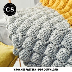 Pode incluir: Um close-up de um cobertor de croch&ecirc; cinza e amarelo com um design texturizado e volumoso. O cobertor &eacute; feito com um fio grosso e tem um visual simples e moderno. O texto "CROCHET PATTERN - PDF DOWNLOAD" est&aacute; na parte inferior da imagem.