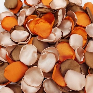 Puede incluir: Un montón de pétalos de flores de seda en tonos marrones, melocotón y naranja. Los pétalos están esparcidos sobre una superficie blanca.