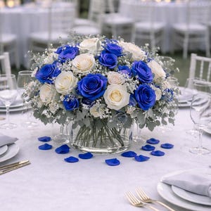 Könnte beinhalten: Eine Tischdekoration mit einem Mittelstück aus blauen und weißen Rosen in einer durchsichtigen Glasvase. Blaue Rosenblätter sind auf der weißen Tischdecke verstreut. Goldene Gabeln und Teller sind für jeden Gast gedeckt.