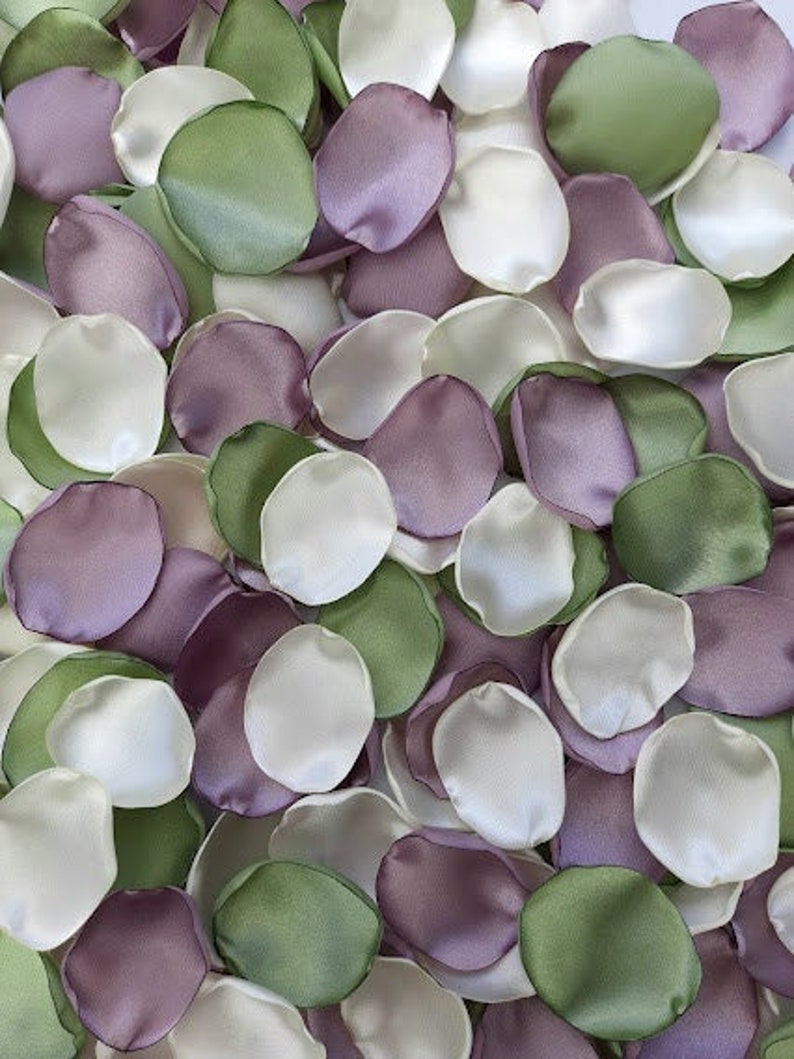 Pu&ograve; includere: Una collezione di petali di fiori di seta in tonalit&agrave; di verde, viola e bianco. I petali sono sparsi su una superficie e sono pronti per essere utilizzati per decorazioni di matrimonio o altri eventi speciali.